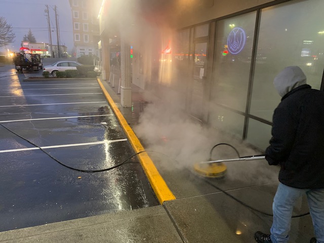 Pressure washing concrete area, a worker uses a surface cleaner. Chinook Services provided this service near Seattle, WA